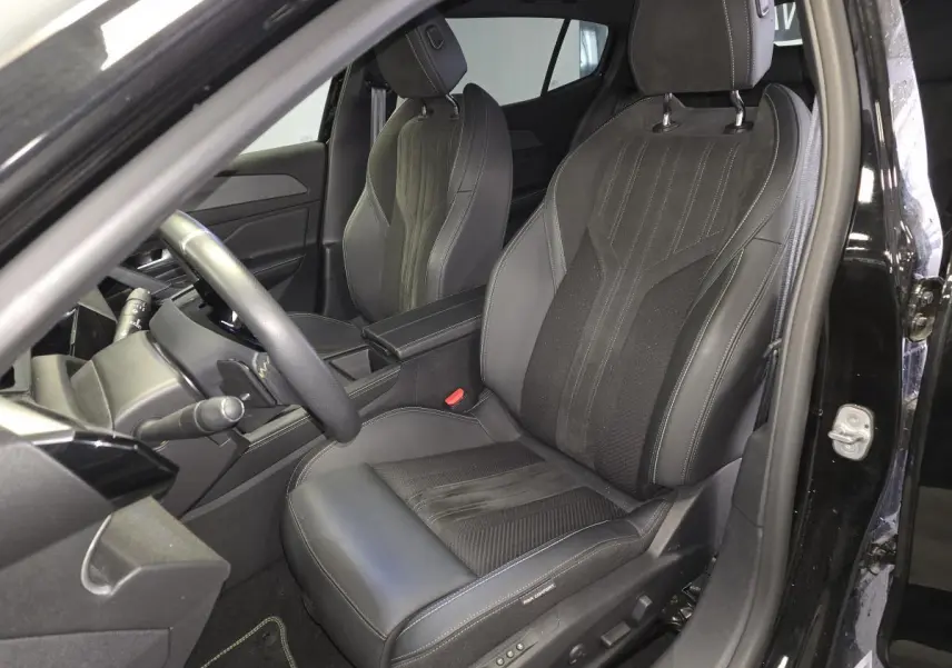 Vue intérieure côté conducteur de la Peugeot 408 GT 1.2i Hybrid 2024, sièges noirs en cuir et tissu avec surpiqûres grises.