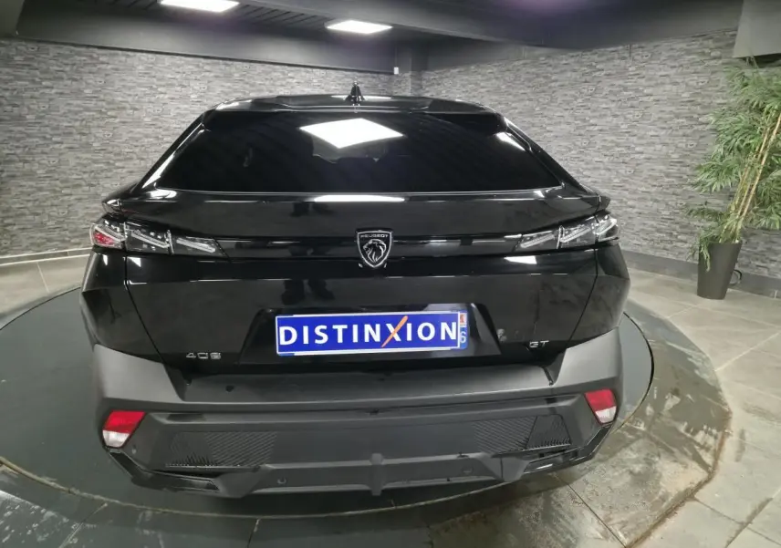 Vue arrière d'une Peugeot 408 noire avec feux arrière fins et logo lion central sur fond noir brillant.