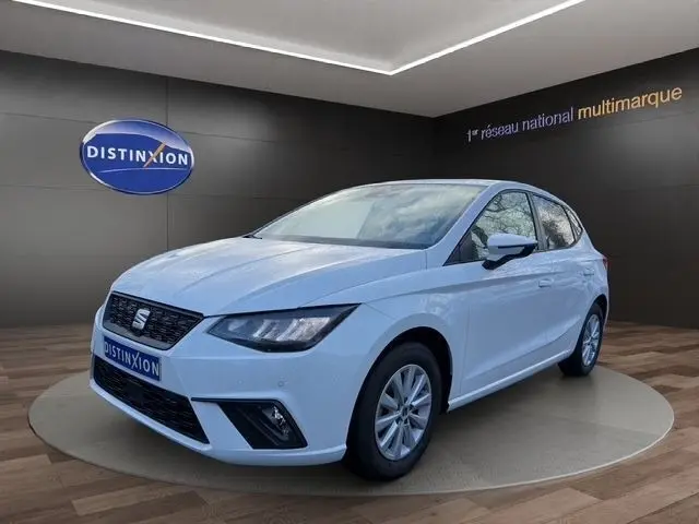 Vue 3/4 avant droite d'une SEAT Ibiza blanche 2023 avec vitres arrière surteintées et feux LED, sur fond showroom.