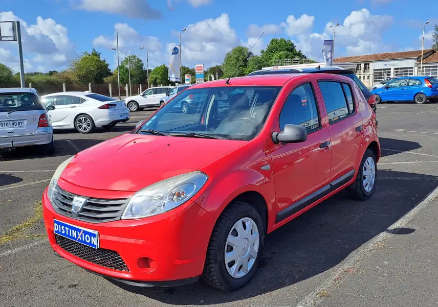 Dacia Sandero rouge vue 3/4 avant droit sur parking, avec jantes acier et rétroviseurs gris.