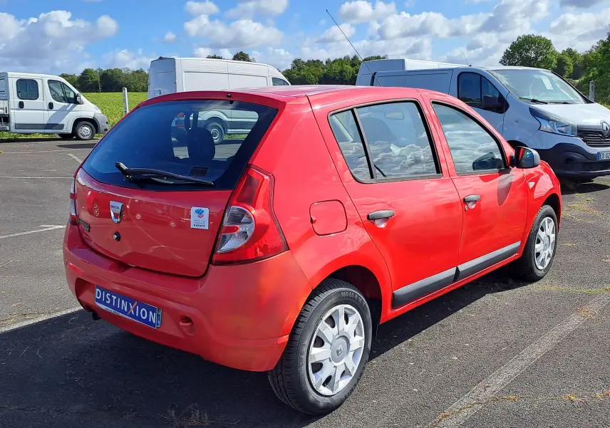 Vue 3/4 arrière droite d'une Dacia Sandero rouge de 2010 avec hayon et jantes argentées, stationnée en extérieur.