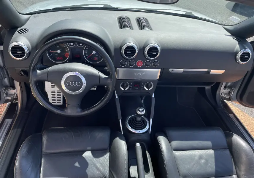 Vue intérieure frontale de l'Audi TT Roadster 1.8T 180 2002, montrant le tableau de bord noir et la boîte manuelle.