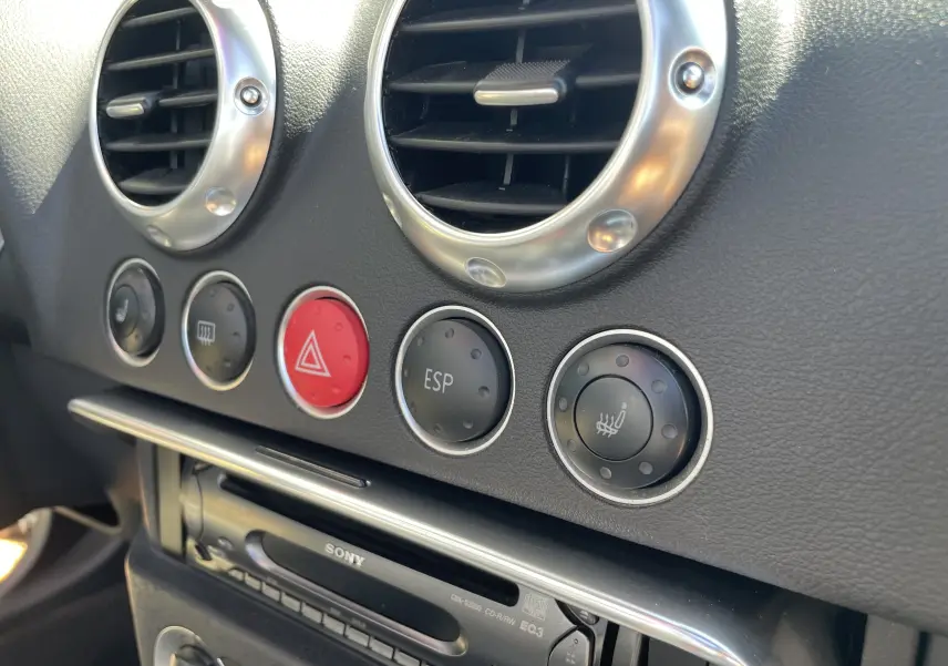 Gros plan sur la console centrale de l'Audi TT Roadster 1.8T 180 gris argent de 2002, montrant les aérateurs ronds et les boutons de contrôle.