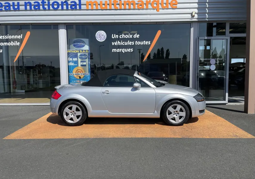 Audi TT Roadster 1.8T 180 gris argent vu de profil côté gauche, capote noire fermée, roues alliage cinq branches.
