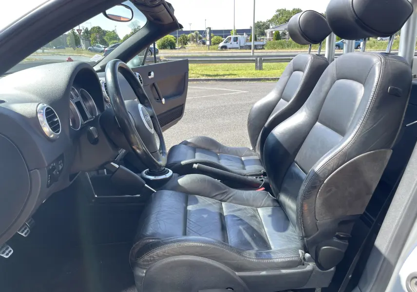 Intérieur de l'Audi TT Roadster 1.8T 180 gris argent 2002, vue côté gauche sur les sièges sport en cuir noir et le volant.