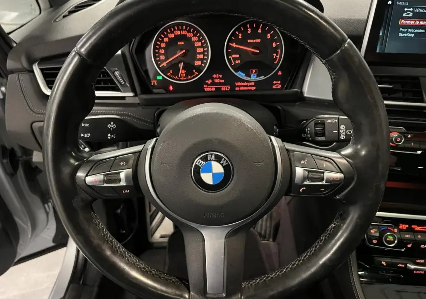 Vue intérieure centrée sur le volant cuir M de la BMW Série 2 225xe gris avec tableau de bord et écran multimédia visibles