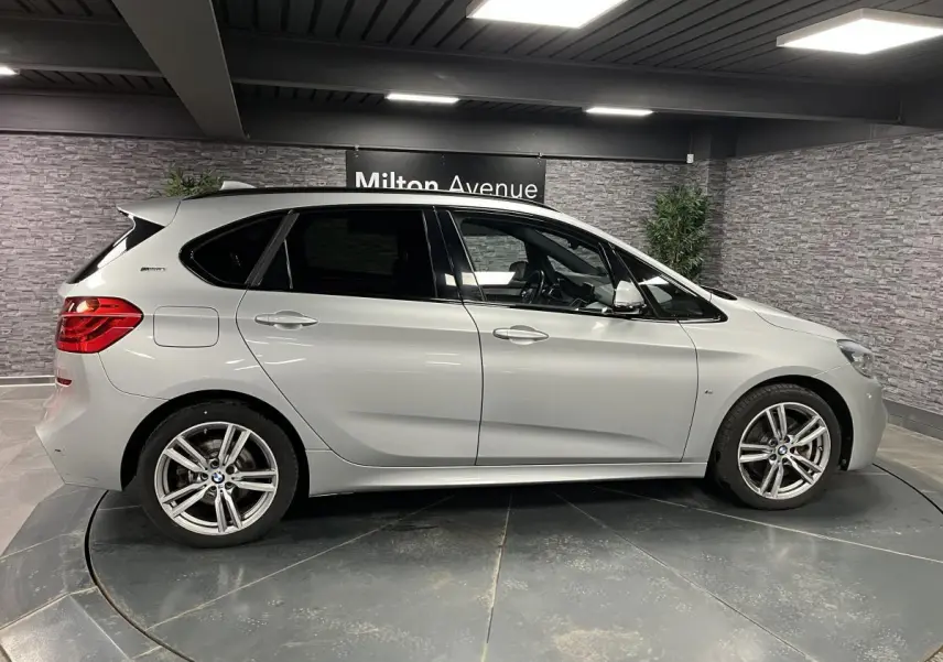 BMW Série 2 225xe Active Tourer gris vue de profil côté gauche en intérieur avec jantes alliage et vitres teintées.