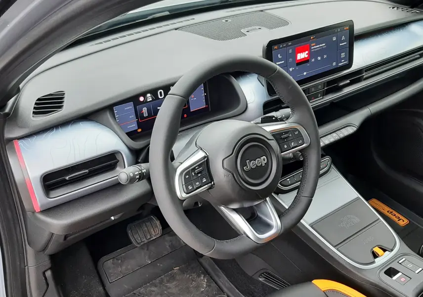 Vue intérieure côté conducteur du Jeep Avenger 2025, tableau de bord gris clair avec volant noir et écran tactile central.