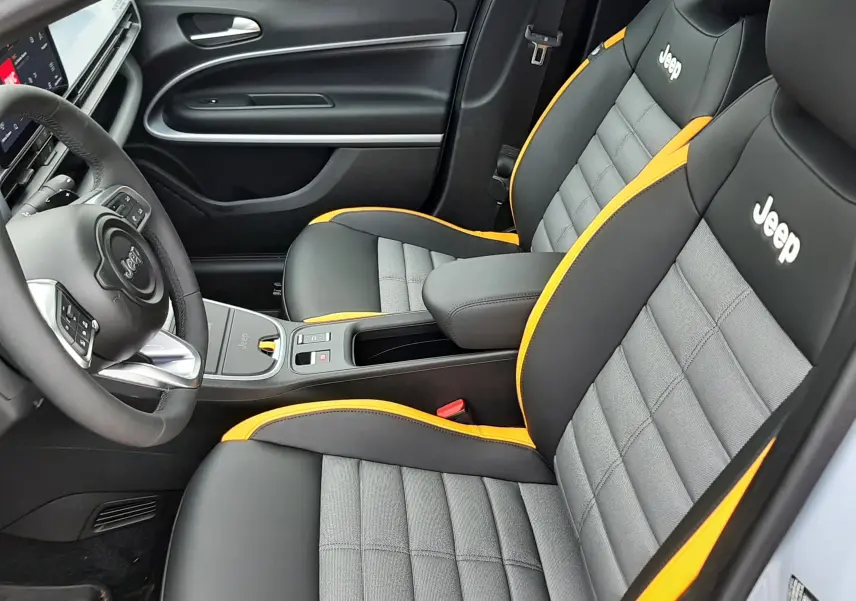 Vue intérieure côté conducteur du Jeep Avenger 2025, sièges gris et noir avec surpiqûres jaunes et logo Jeep brodé.