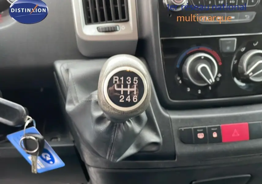 Gros plan sur le levier de vitesses manuel 6 rapports du Fiat Ducato Fourgon blanc, avec tableau de bord et commandes de climatisation visibles.