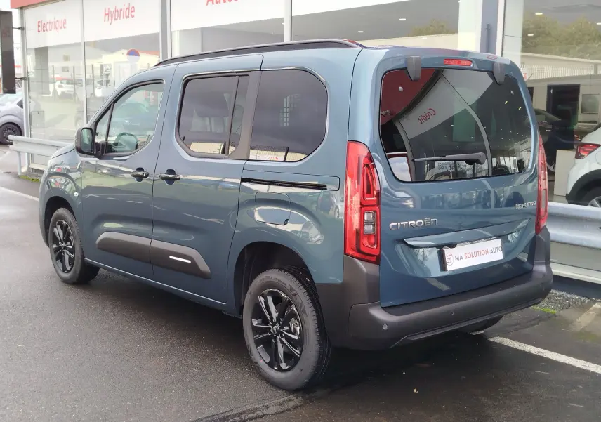 Vue 3/4 arrière droite d'un Citroën Berlingo bleu Kiarma avec vitres teintées et jantes noires.