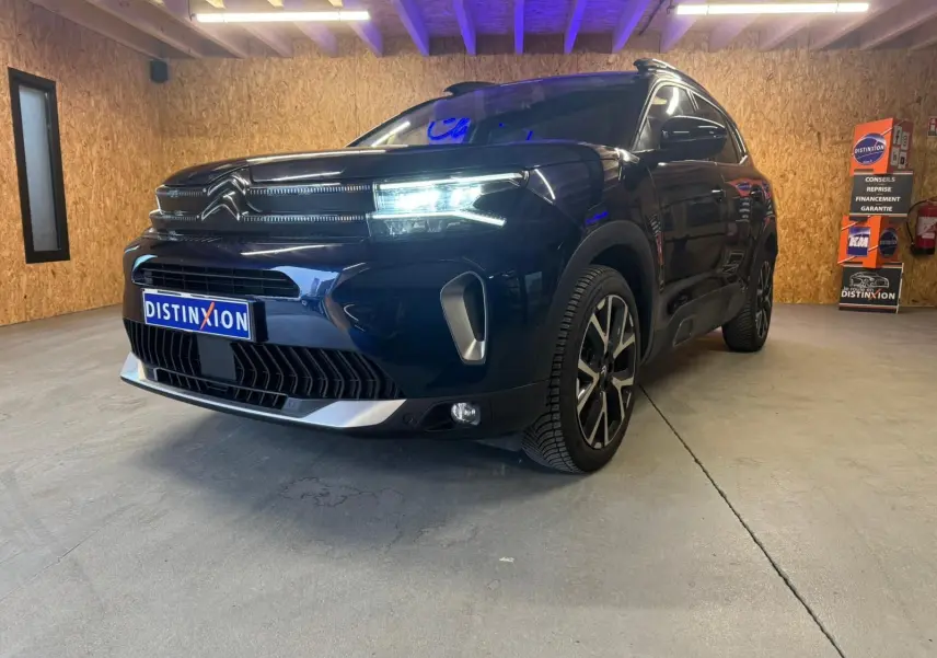 Vue 3/4 avant droite du Citroën C5 Aircross bleu avec barres de toit et jantes alu 18 pouces dans un showroom.