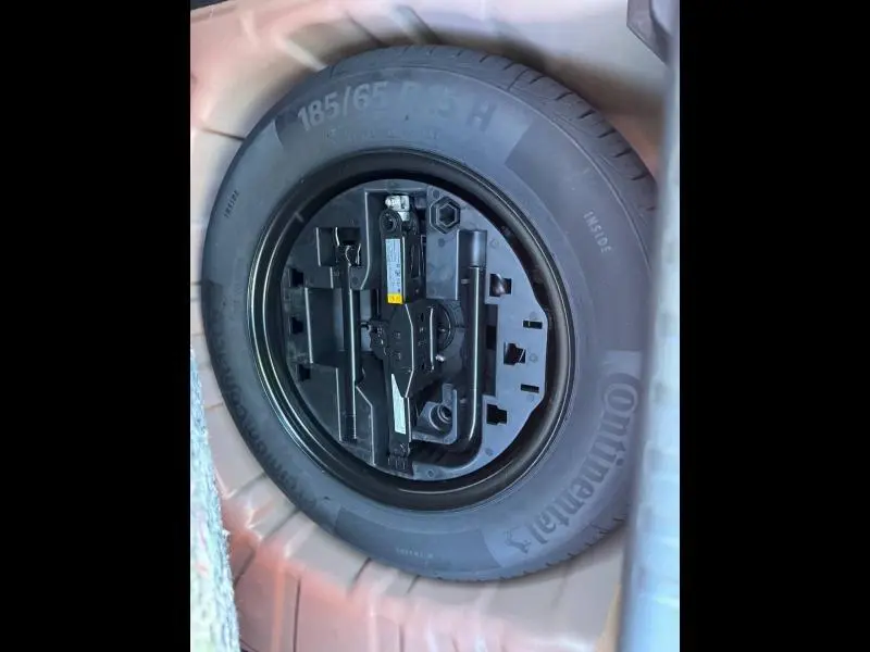 Pneu de secours Continental noir avec outils de bord dans le coffre d'une Renault Clio orange Valencia 2025.