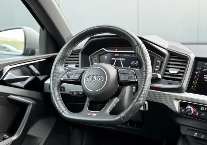 Volant sport multifonctions en cuir perforé de l'Audi A1 Sportback 30 TFSI 2023, avec tableau de bord numérique et détails noirs.