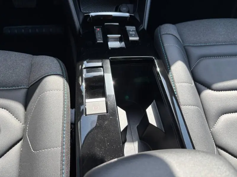 Vue rapprochée de la console centrale noire entre les sièges tissu gris du Citroën C4 X 2024.