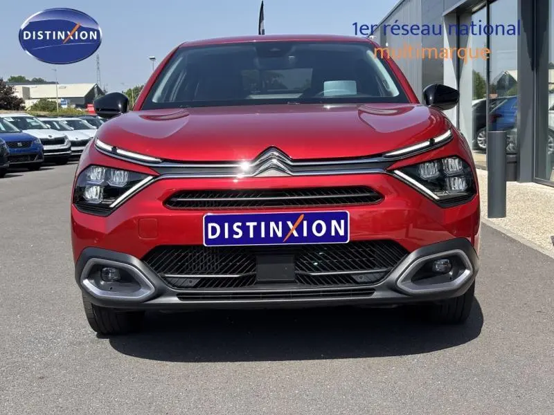 Vue frontale d'une Citroën C4 X rouge Elixir avec phares LED et calandre chromée sur parking extérieur.