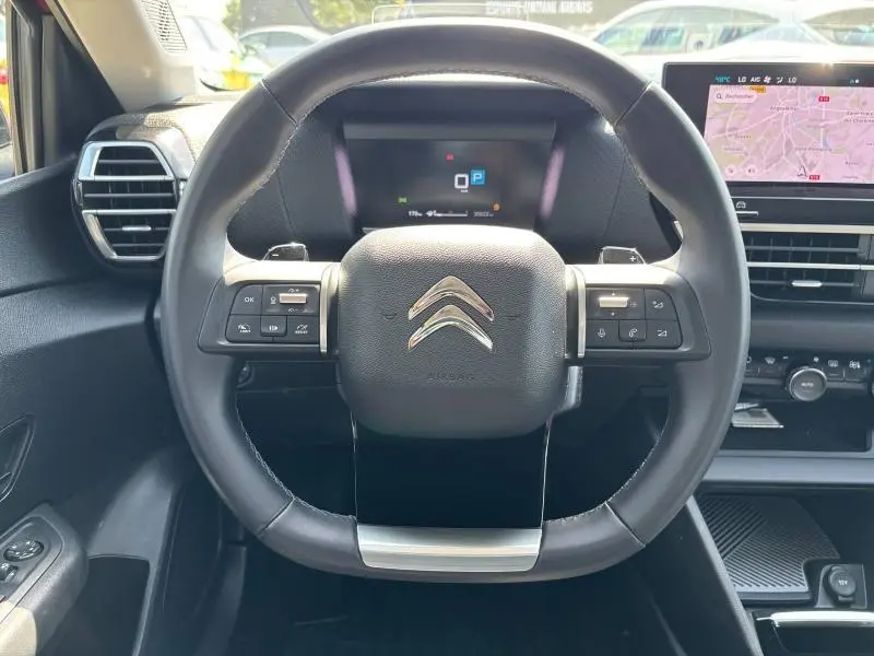 Volant cuir de la Citroën C4 X 2024 vu de face, avec commandes intégrées et tableau de bord numérique en arrière-plan.