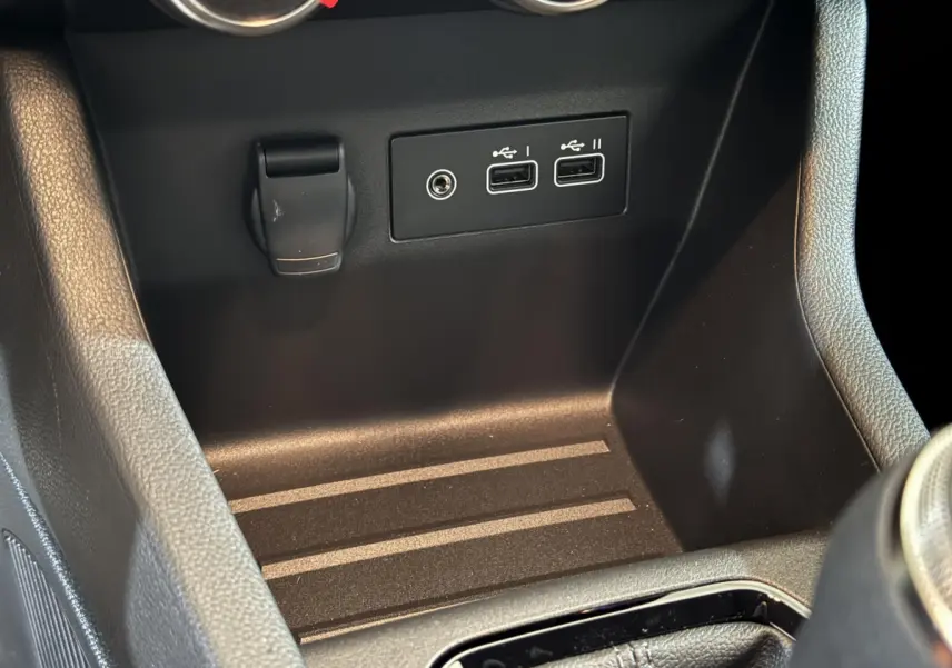 Vue rapprochée de la console centrale noire de la Renault Clio avec prises USB et prise 12V visibles.