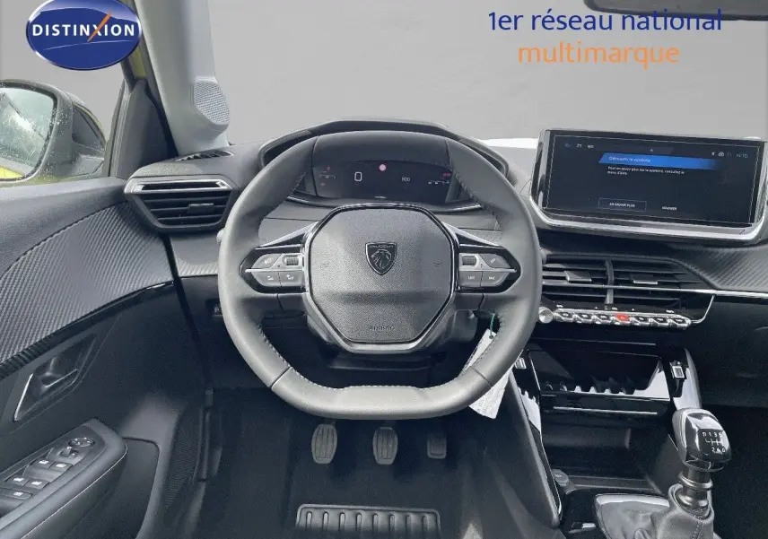 Vue intérieure centrée sur le volant et la console d'une Peugeot 208 jaune Agueda Metal, boîte manuelle visible.