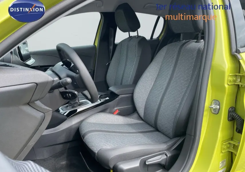 Vue intérieure côté conducteur d'une Peugeot 208 jaune Agueda Metal, montrant les sièges gris et la console centrale.