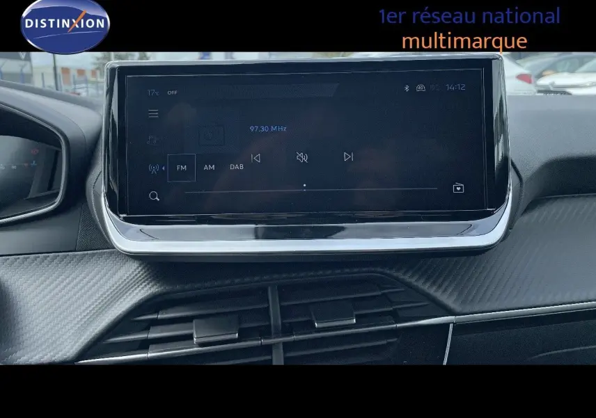 Écran tactile central du tableau de bord de la Peugeot 208 2025, affichant la radio FM, intérieur noir.