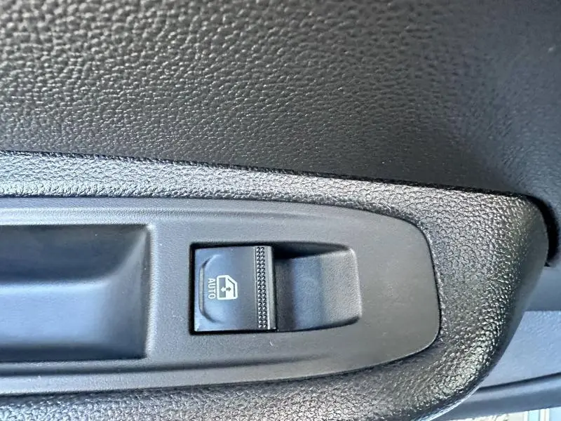 Gros plan sur le bouton de commande de la vitre électrique avant gauche dans l'intérieur noir texturé de la Renault Clio Gris Rafale 2025.