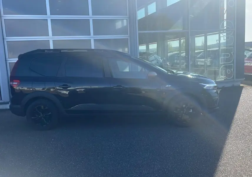 Profil côté gauche du Dacia Jogger noir nacré 2024, avec barres de toit et jantes alu noires visibles.