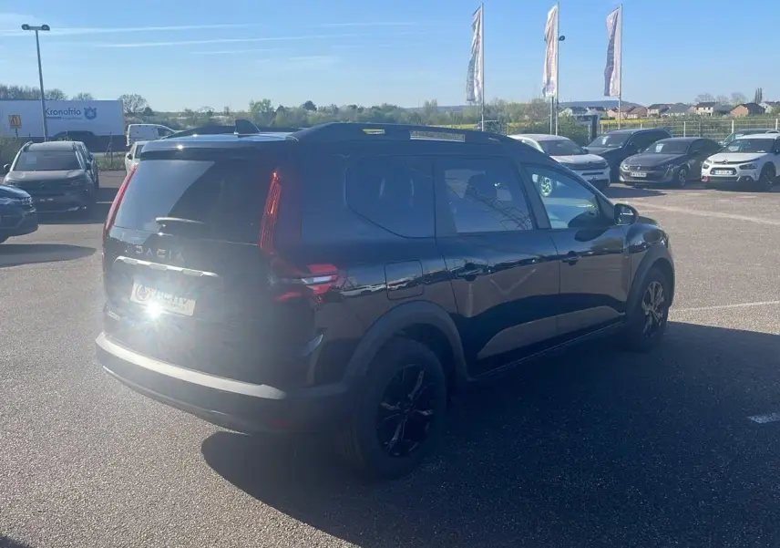 Vue 3/4 arrière droite d'un Dacia Jogger noir nacré avec barres de toit et jantes noires sur parking.