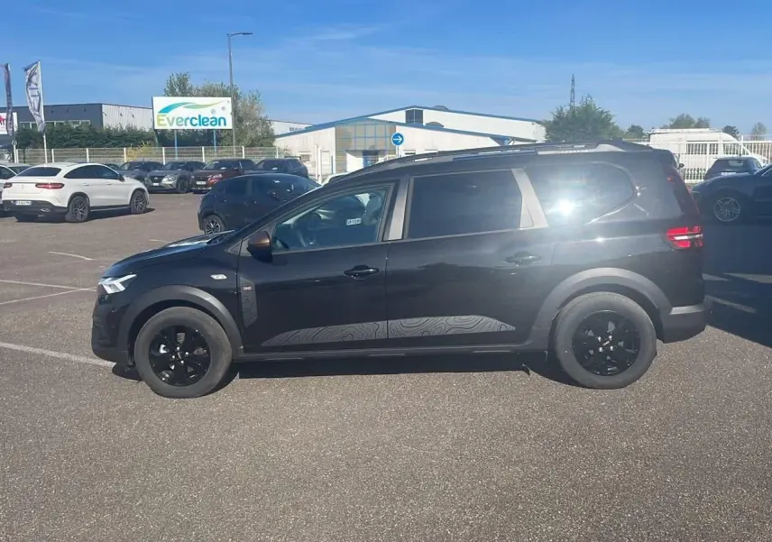 Dacia Jogger 2024 noir nacré vu de profil côté gauche, avec barres de toit et jantes noires.