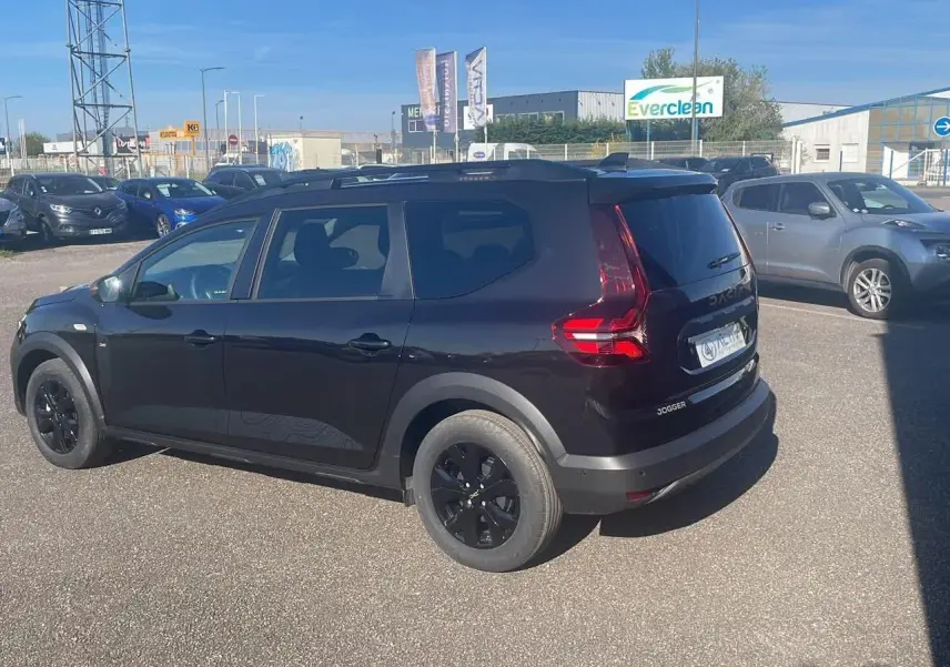 Dacia Jogger noir nacré vue 3/4 arrière droit, avec jantes noires et barres de toit visibles.