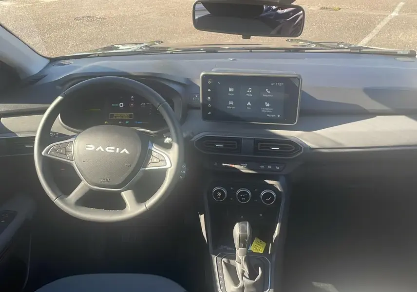 Vue frontale de l'habitacle du Dacia Jogger 2024 avec volant, écran tactile et levier de boîte automatique.