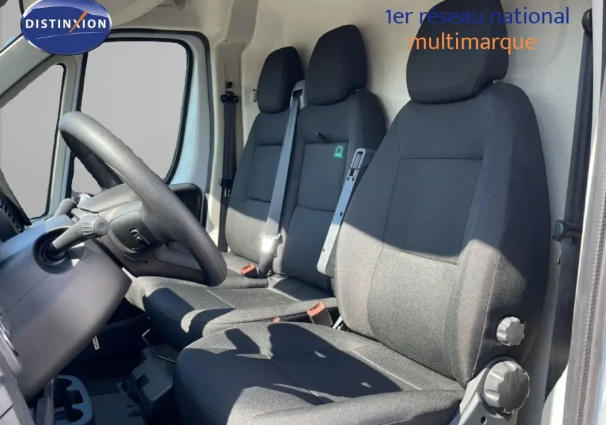Vue intérieure côté conducteur du Peugeot Boxer Fourgon blanc banquise, montrant les sièges noirs et le volant.