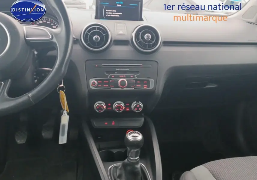 Vue intérieure centrée sur le tableau de bord et la console centrale d'une Audi A1 blanche avec boîte manuelle.