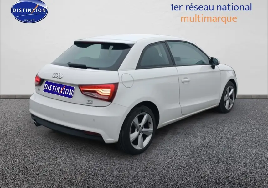 Audi A1 blanc vue 3/4 arrière droit, feux arrière allumés et jantes alliage cinq branches.