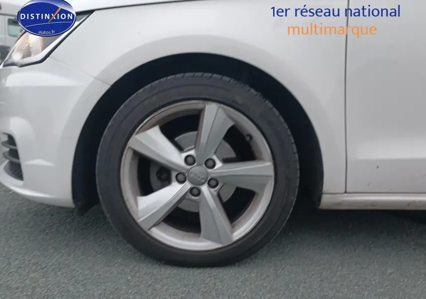 Gros plan sur la roue avant gauche d'une Audi A1 blanche, jante alliage cinq branches visible.