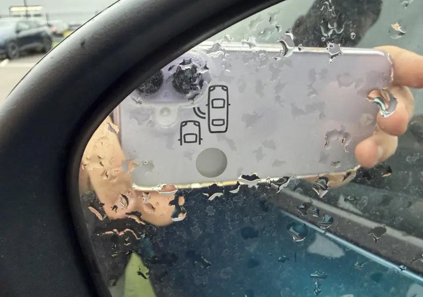 Rétroviseur gauche d’un Renault Arkana bleu Zanzibar, avec icône d’alerte d’angle mort visible sous la pluie.
