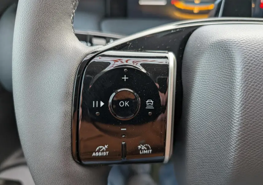 Gros plan sur les commandes noires du volant gris du Citroën C5 Aircross hybride, avec boutons multifonctions et symbole d'assistance.
