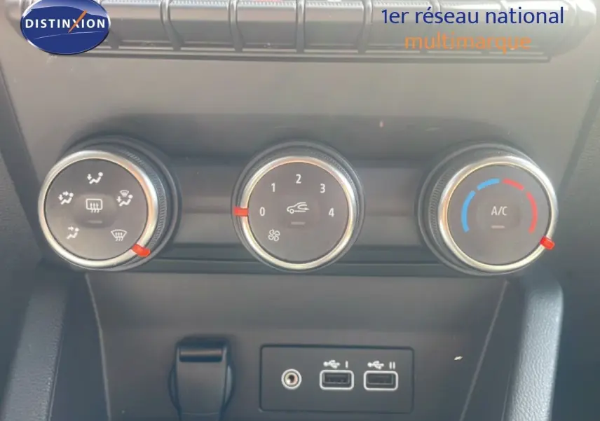 Gros plan sur les commandes de climatisation et ventilation d’une Renault Clio blanche, avec boutons ronds et ports USB visibles.