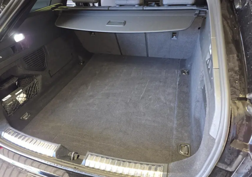 Coffre ouvert vu de l'arrière d'une Audi A5 Avant noir avec tapis de sol et cache-bagages déployé.
