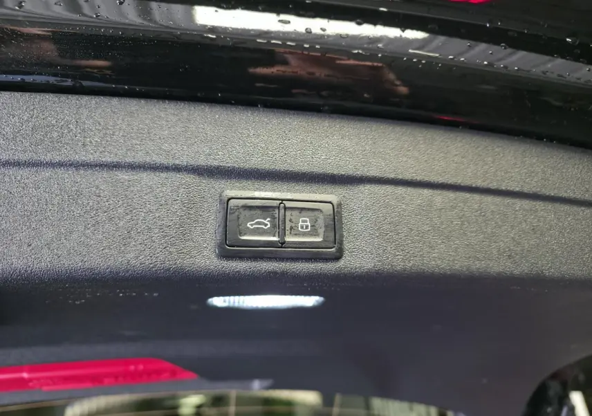 Gros plan sur les boutons d'ouverture et de verrouillage du hayon d'une Audi A5 Avant noire, vue intérieure du coffre.