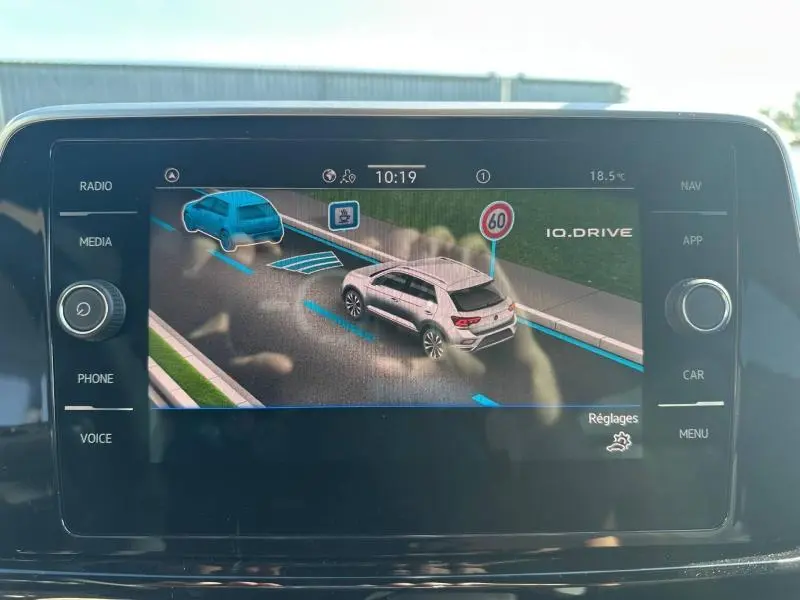 Écran tactile du système de navigation Volkswagen montrant une voiture blanche en 3/4 arrière et un panneau 60 km/h.