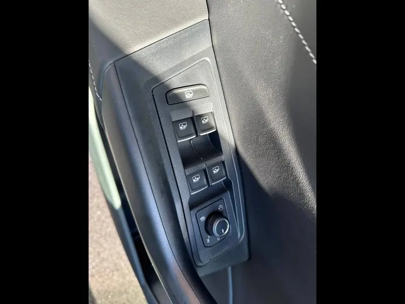 Gros plan sur les commandes de lève-vitres et réglage des rétroviseurs côté conducteur, garniture noire intérieure.