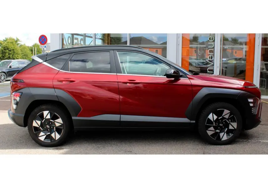 Hyundai Kona 2024 rouge Ultimate Metal avec toit noir, vue profil côté gauche, jantes alliage et protections noires.