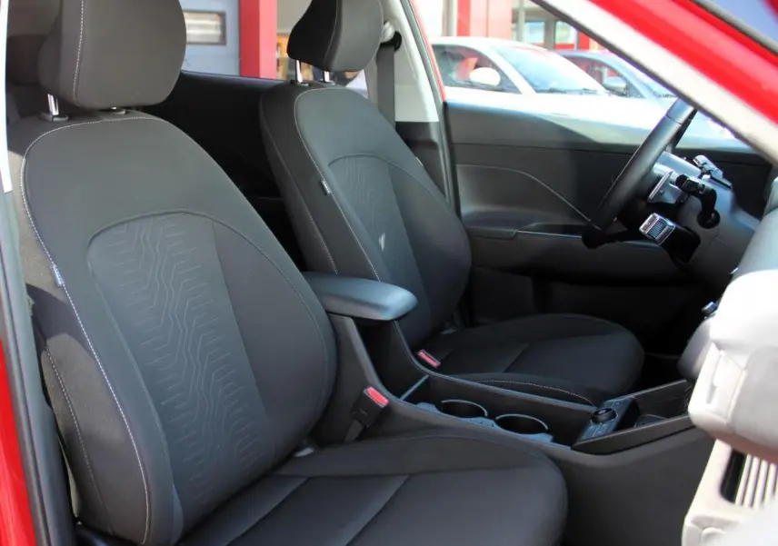 Vue intérieure côté avant droit du Hyundai Kona 2024 rouge Ultimate Metal, montrant les sièges noirs et l'accoudoir central.