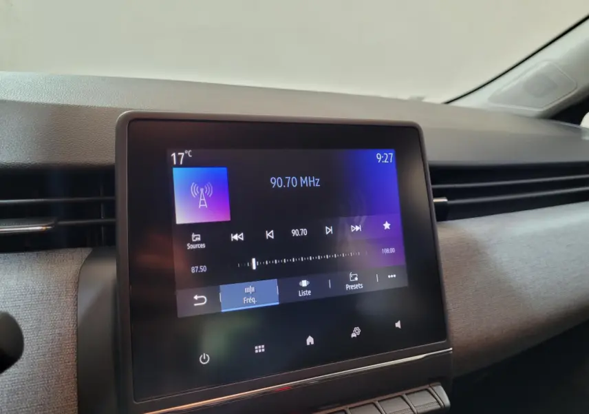 Écran tactile central de la Renault Clio gris foncé 2025 affichant la radio FM à 90,70 MHz, vue intérieure de profil droit.