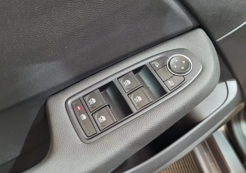 Gros plan sur les commandes de lève-vitres et rétroviseurs sur la porte côté conducteur d’une Renault Clio gris foncé.