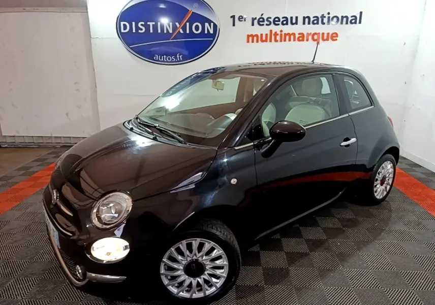 Vue 3/4 avant droit d'une Fiat 500 noire brillante avec jantes argentées dans un showroom intérieur.
