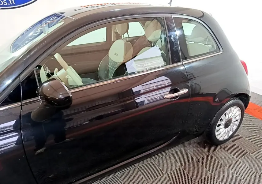 Vue de côté droit d'une FIAT 500 noire 2019 avec intérieur clair et jantes alliage distinctives.
