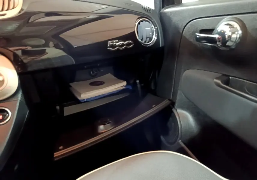 Vue intérieure côté passager de la Fiat 500 noire, montrant la boîte à gants ouverte et le tableau de bord brillant.