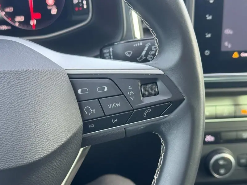 Gros plan sur les commandes multifonctions du volant cuir noir du SEAT Ateca 2024, avec coutures blanches visibles.
